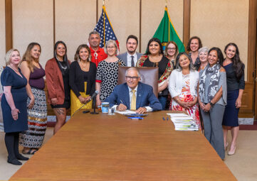 A group of people gathered around Gov. Jay Inslee at the end of a boardroom table for signing ceremony.