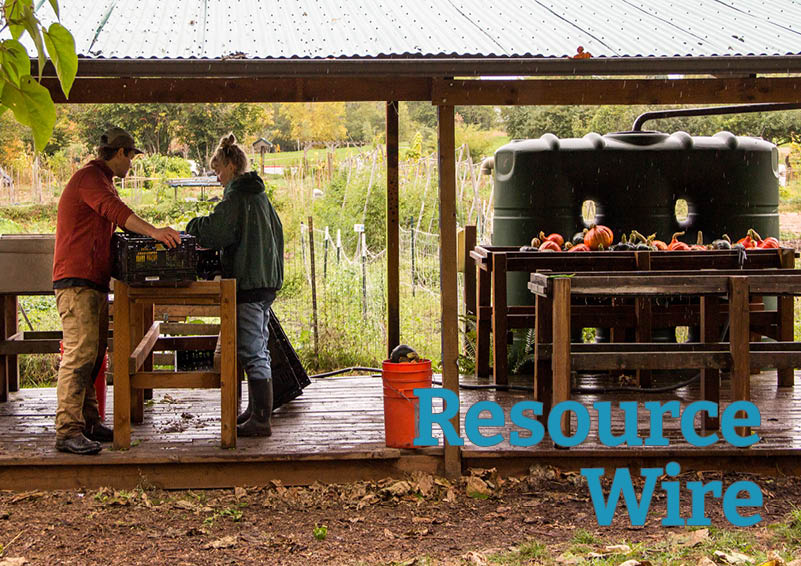 Two people clean freshly harvested vegetables under a rain shelter with fields in the background. The words "Resource Wire" appear beside them.