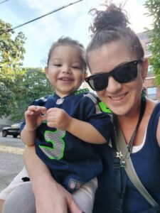 A woman in sunglasses holds her young son, who is wearing a tiny football jersey.