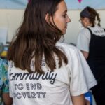 The back of a young woman whose tshirt reads "Building community to end poverty."