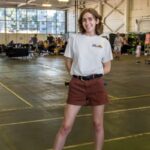 A young woman with a Solid Ground tshirt wearing roller blades in an airplane hangar.