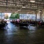 A wide shot of people at tables in a large airplane hangar.