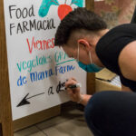 A Sea Mar health educator writes a sign on a white board that says "Food FARMacia" with a welcome in Spanish.