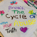 A white shirt painted with pictures of a heart, butterfly, and flowers, along with the phrases, "Break the cycle of abuse," and "Know your truth."