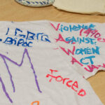 A close up of a T-shirt sleeve that has been painted with the words "Violence Against Women Act," and "Established 1990."