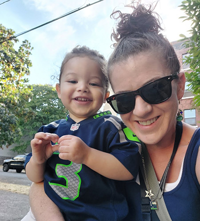 A woman in sunglasses holds her young son, who is wearing a tiny football jersey.