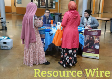 Two women in colorful dresses and headscarves talk to a man and woman seated at table with various things on it. A sandwich board that reads "Rent Smart" is next to the table. The words "Resource Wire" appear at the bottom of the page.