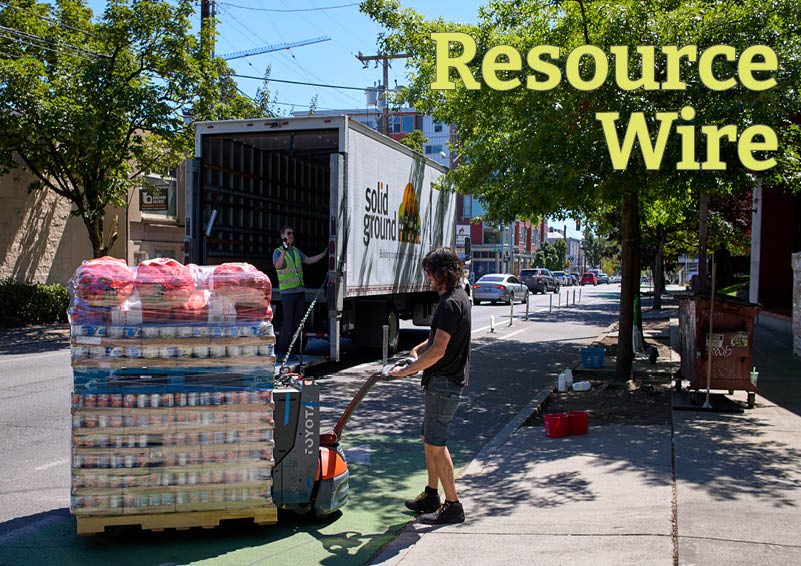 One man moves a crate stacked high with packaged food while another man gestures from inside a semi-truck that says "Solid Ground" on the side. The words Resource Wire appear above them.