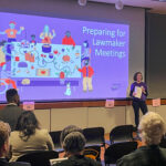 A woman gives a presentation next to a large projection of an illustration of several different people gathered around a table and the words "Preparing for Lawmaker Meetings."