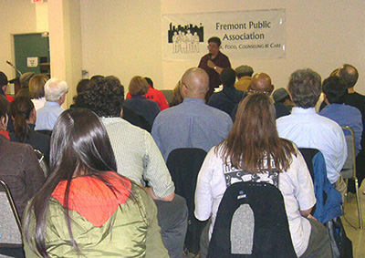 A grainy photo of a woman addressing an audience in front of a banner that reads "Fremont Public Association."