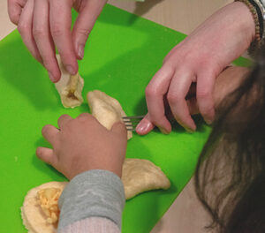 A close up a child's hands as they use a fork to shape pierogi with the help of an adult.
