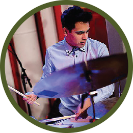 Circular photo with a forest-green frame of a man with dark brown hair playing drums. He's wearing a light blue button-down shirt.