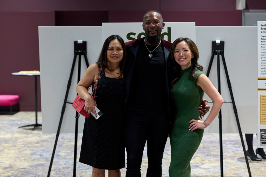 A man in a suit and two women in dresses post for a photo.