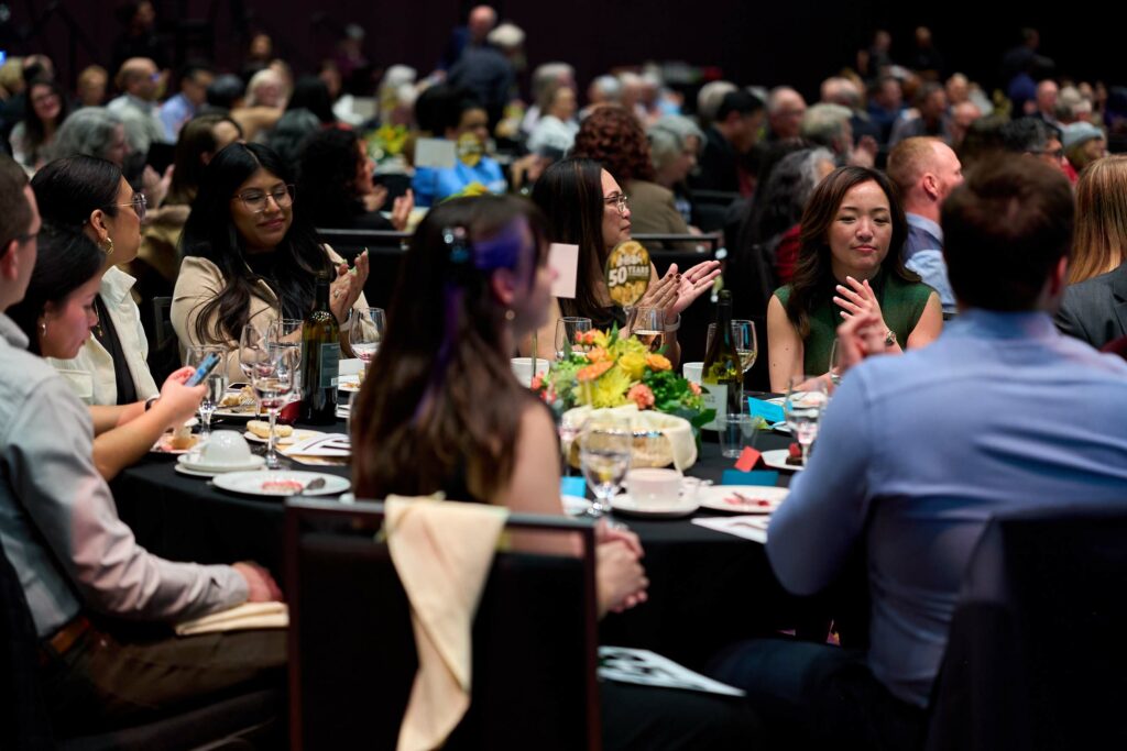 A crowd of well-dress people sitting around tables at a gala.