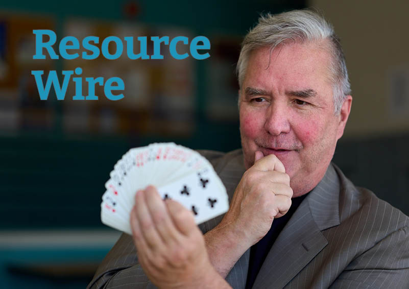 A man with gray hair holds a deck of cards fanned open and facing away from him, as if asking someone to pick a card. The words "Resource Wire" appear above him.