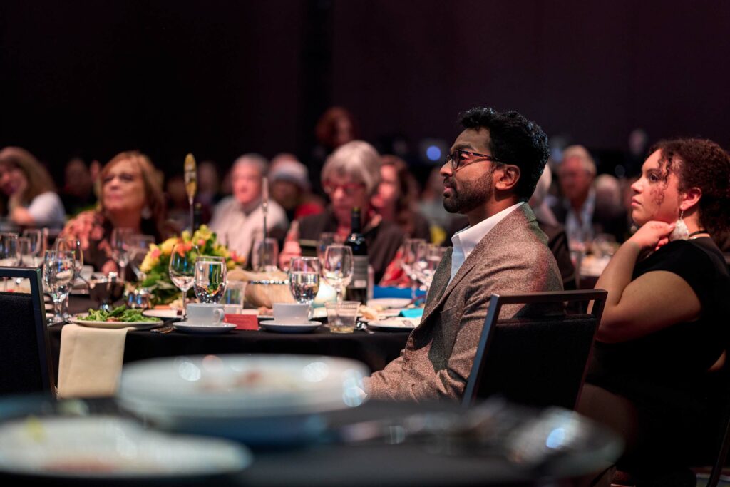 A man among a crowd of people at a gala watches something out of frame .