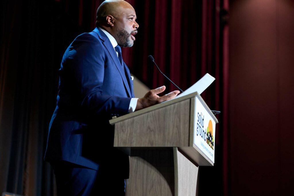 A man in a blue suit at a podium that says "Solid Ground."