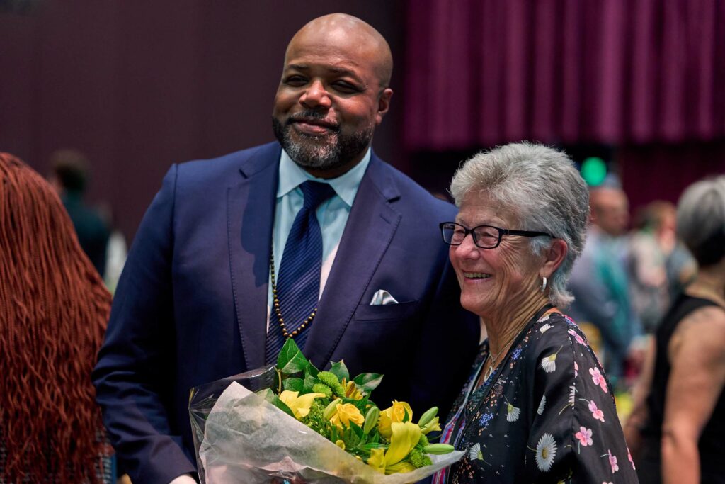 A man in a blue suit and tie next to an older woman holding a bouquet of yellow flowers.