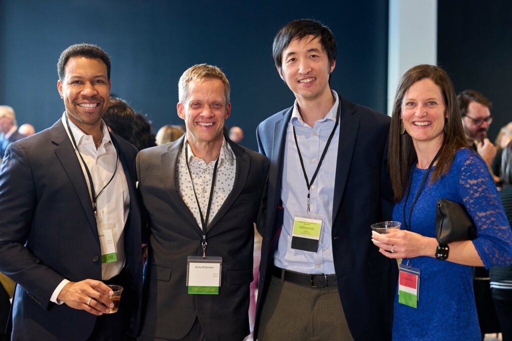 Four people wearing nametags on lanyards around their necks pose for a photo.