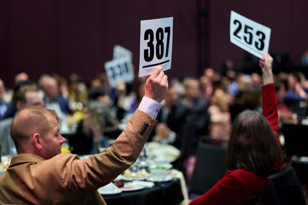 Several people in a crowd hold up bid cards with different numbers.