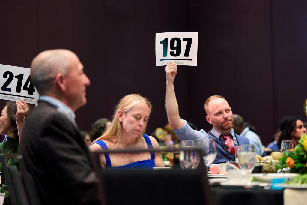 Several people in a crowd hold up bid cards with different nuimbers.