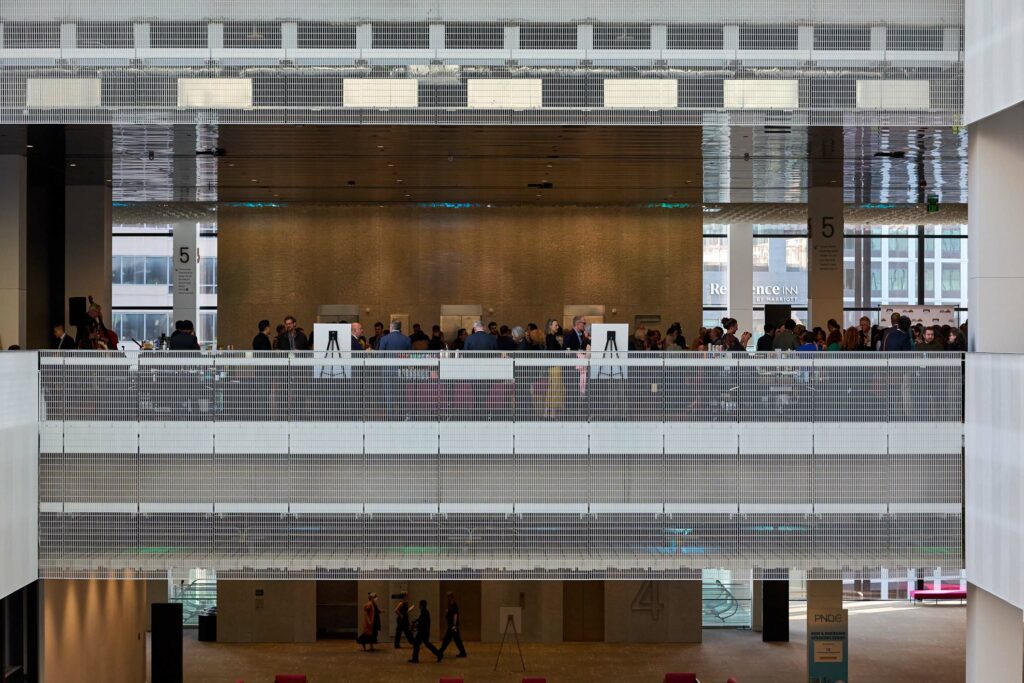 A crowd of people seen from a distance through the atrium of a convention center.