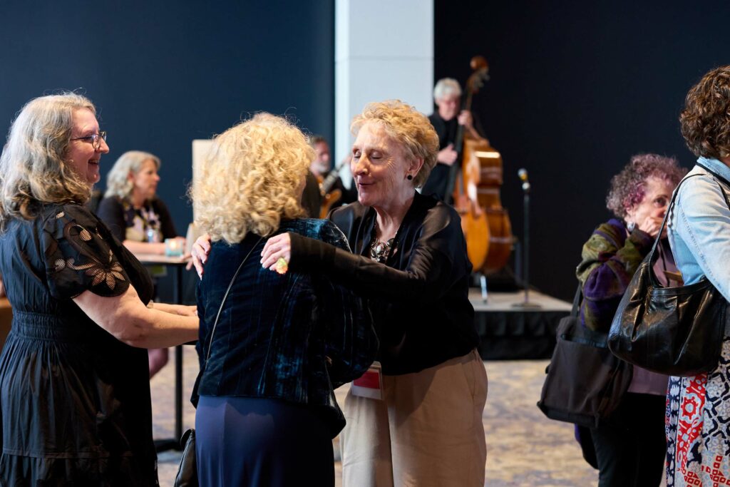 Two women embrace as a musician plays upright bass in the background.