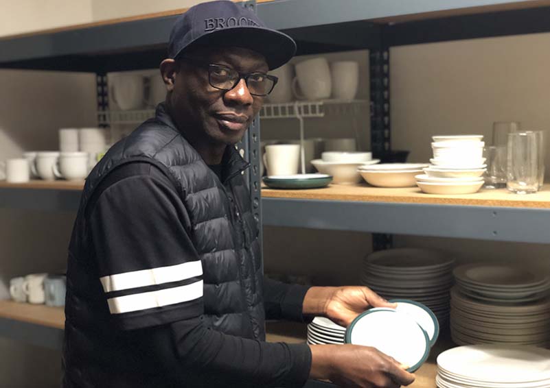 A man with a black sweater and cap holds a few dishes from two racks full of dishware.