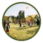 Circular photo with a dark green border of a gravel path winding through a park with trees and, a boulder, and a picnic table in the background.