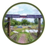 Circular photo with a dark green border of a painted wooden archway that reads Solid Ground Giving Garden. Through the arch you can see a woodchip path and rows of vegetables.