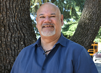 Portrait of man in a blue shirt standing in front of a large tree.