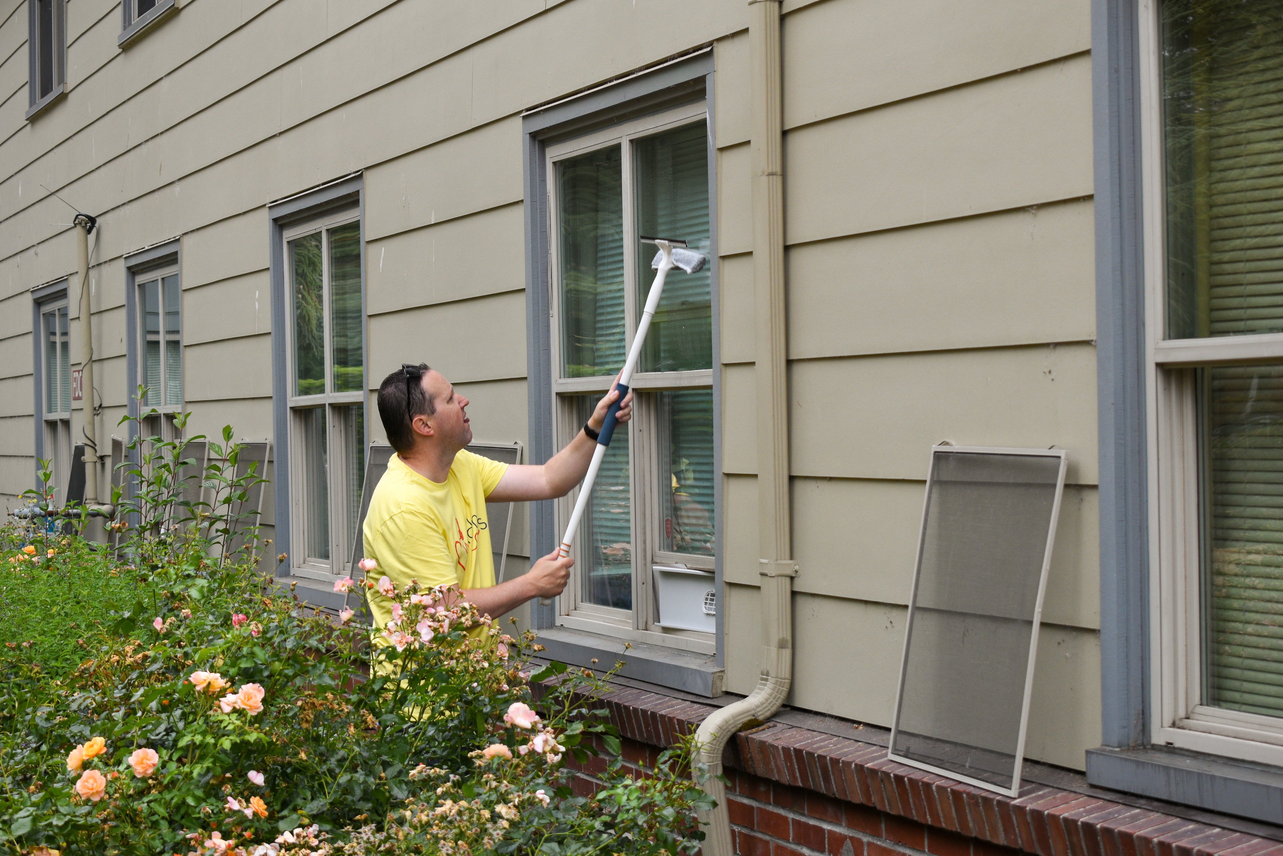 A man in a yellow t-shirt stands outside a building washing windows