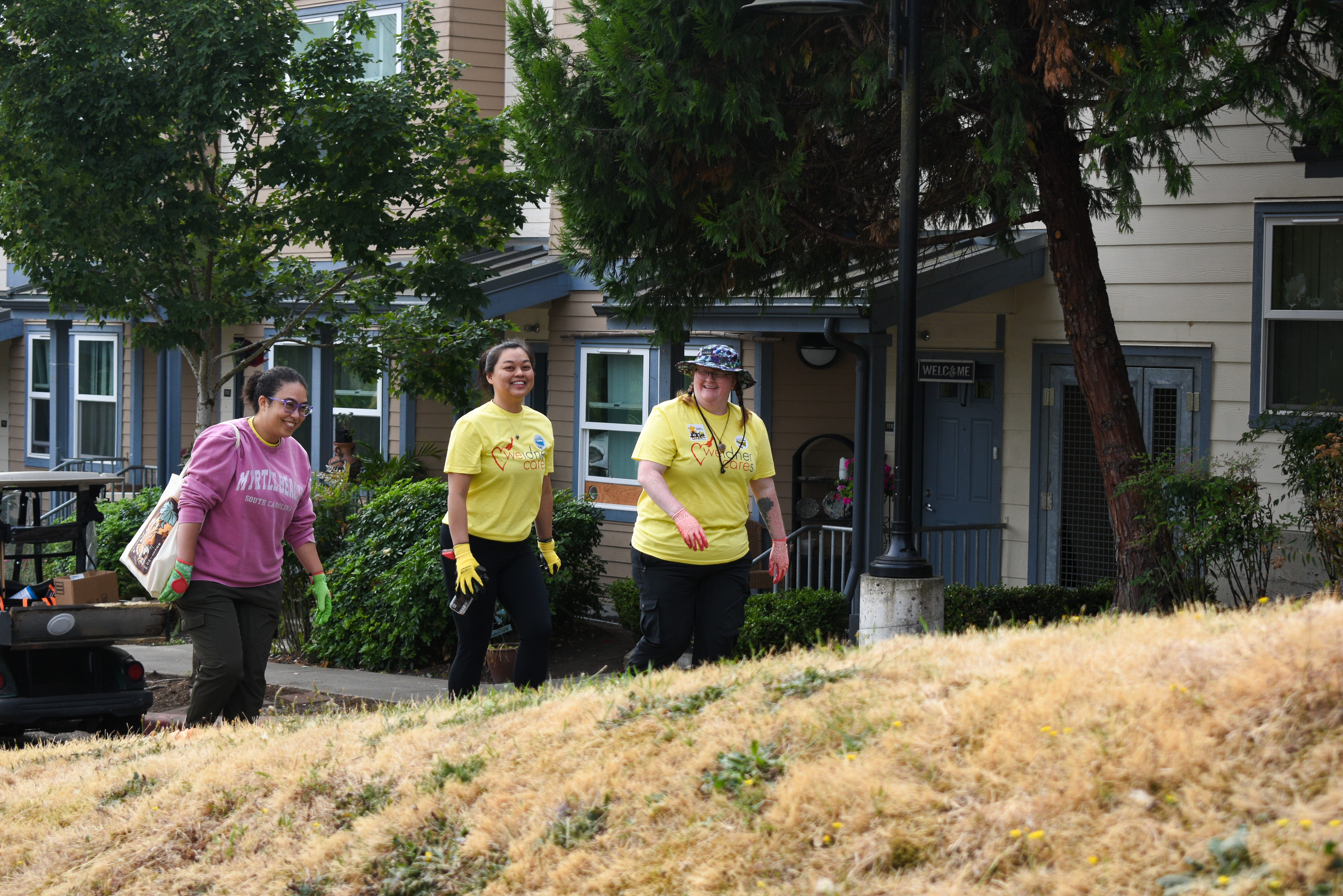 Three volunteers wearing work gloves walk past an apartment building