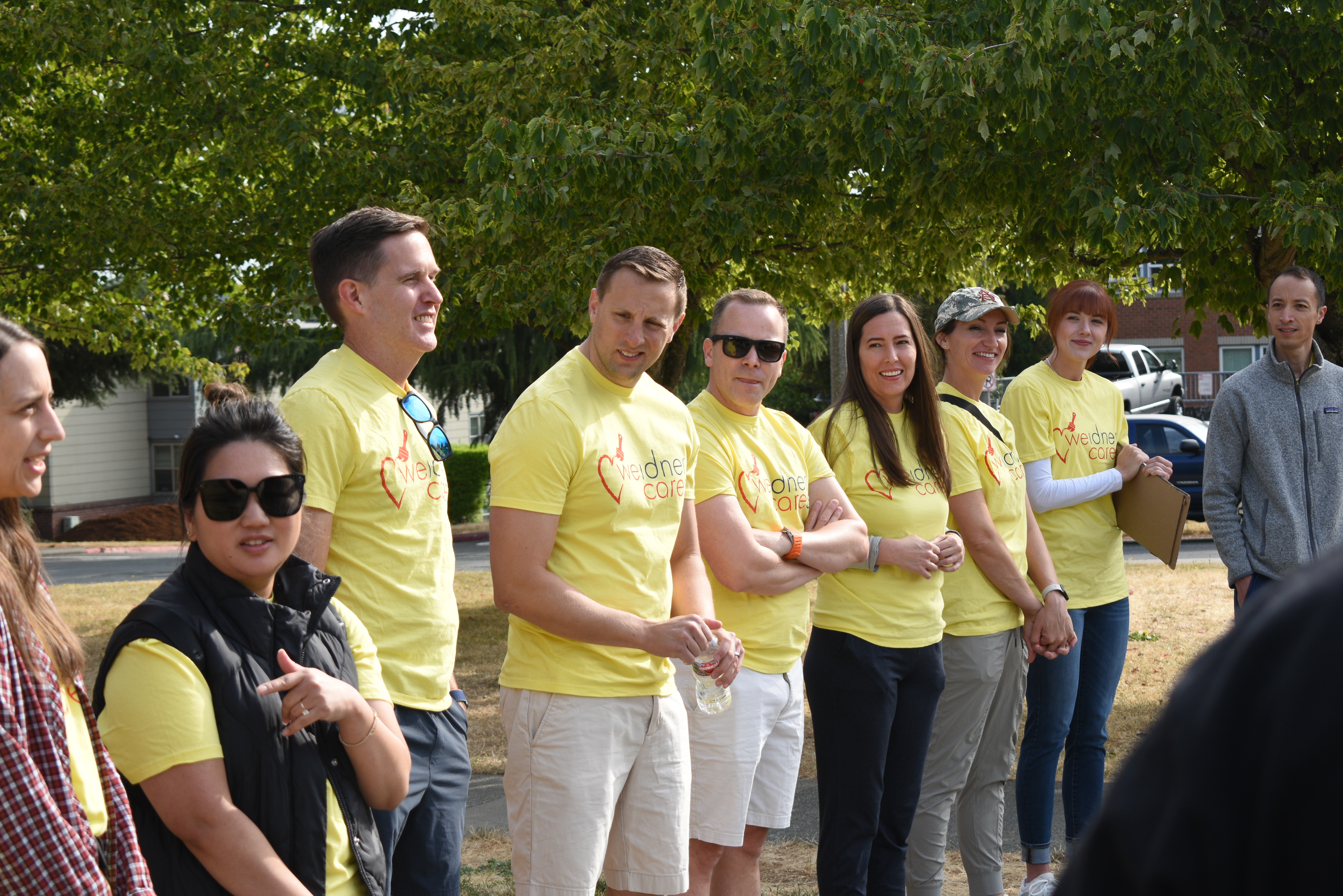 A group of people in yellow shirts stand should to shoulder in a row