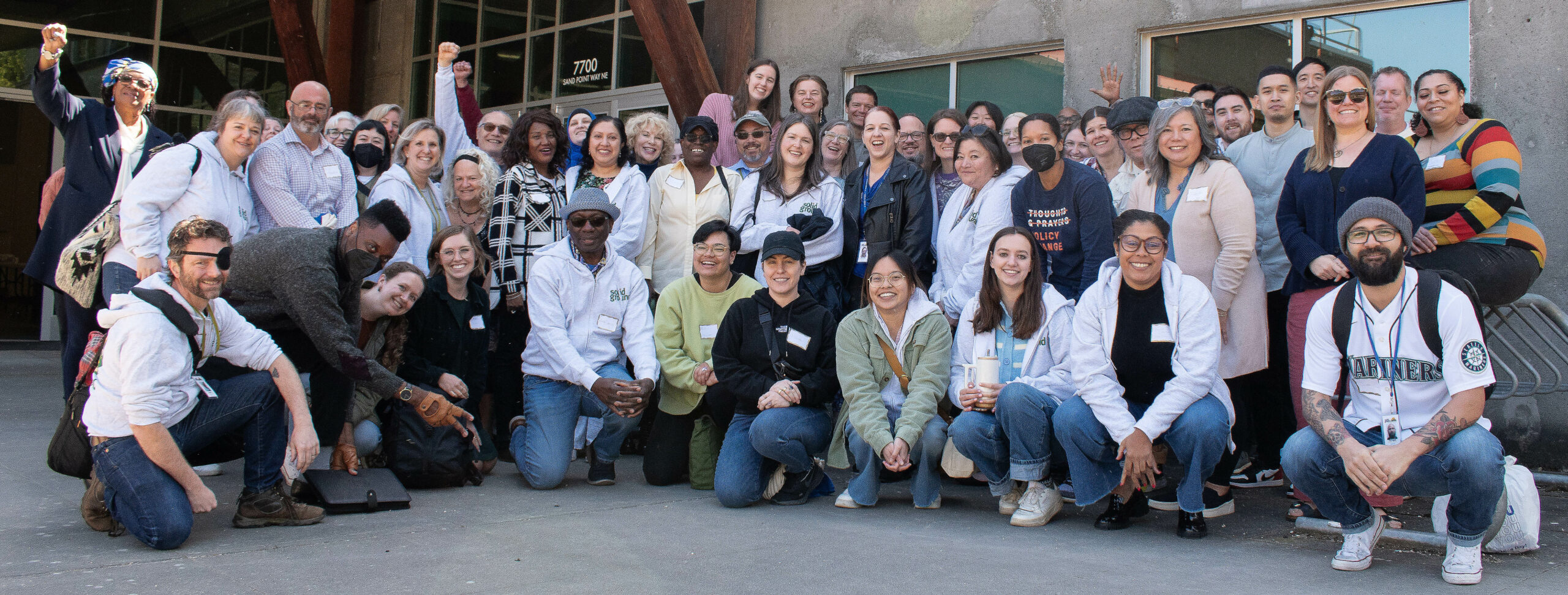 Large group of Solid Ground staff smiling and posing outside a building on a concrete floor.