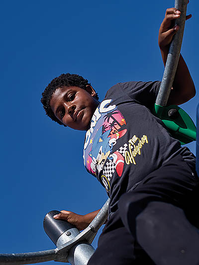 A young Black boy on a jungle gym with a deep blue sky above him.