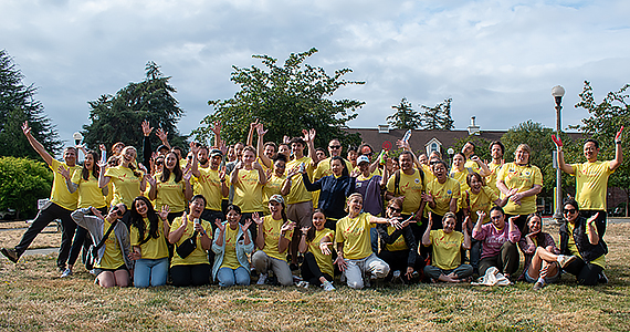 Large group of people wearing light-yellow T-shirts, waving and cheering.