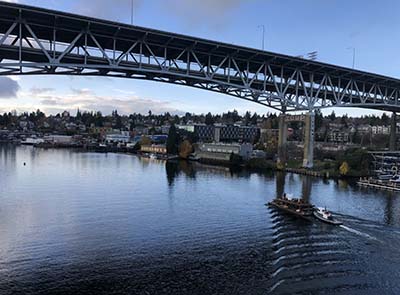 A tug boat pushes a heavily loaded barge under a tall bridge.