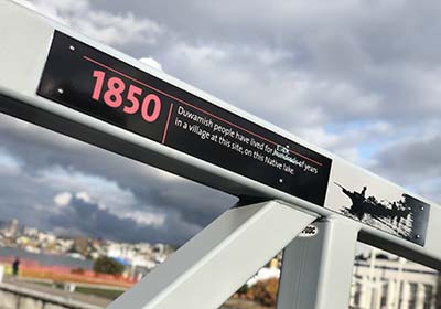 A picture of a sign on a bridge that says "1850: Duwamish people have lived here for hundreds of years in a village at this site, on this Native Lake.