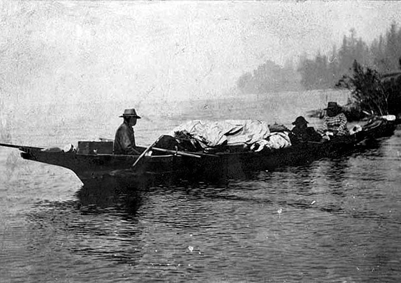 A grainy, black-and-white photo of several men in heavily loaded canoe.