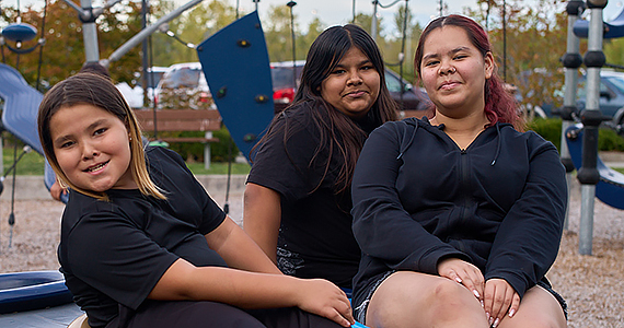 Three youth/teen kids pose together on a playground.