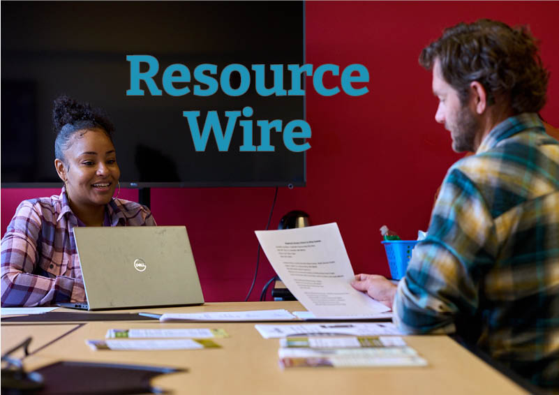 A man in a blue plaid shirt holds a piece of paper and talks to a woman behind a laptop wearing a pink plaid shirt. The words "Resource Wire" appears between them.