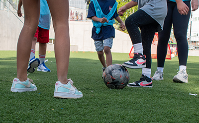 A cropped shop showing the legs of adults and kids practicing soccer drills on a synthetic turf field.