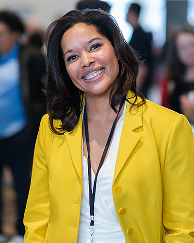 Portrait of a Black woman with straight, shoulder length hair, wearing a bright yellow blazer and a white blouse.