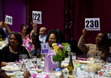 Several people gathered at a table raise bid cards.