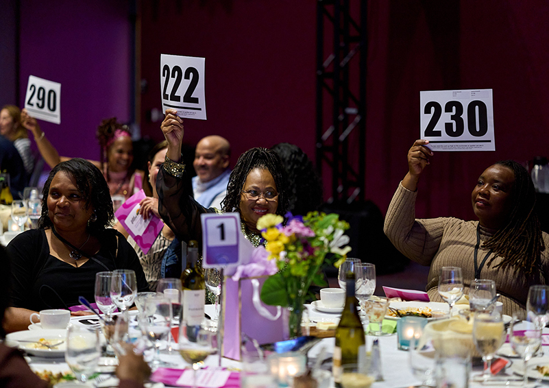 Several people gathered at a table raise bid cards.