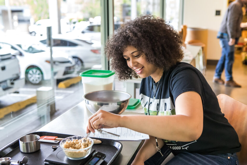 A cooking class student carefully weighs ingredients on a digital scale.