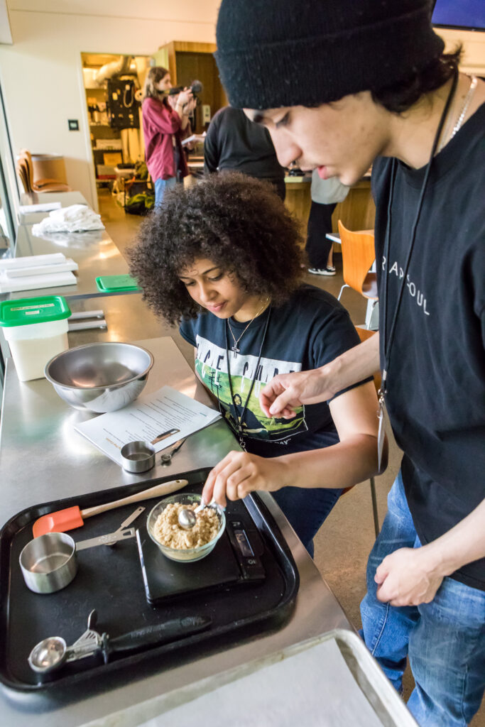 Two cooking class students weigh and mix ingredients.