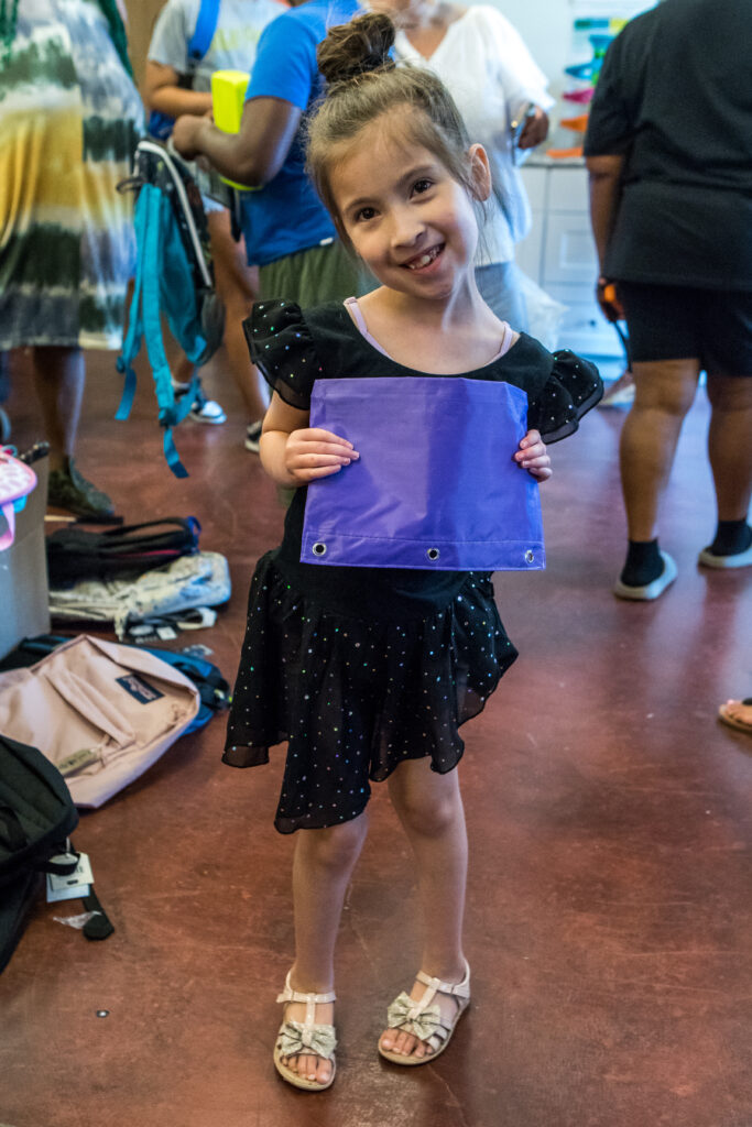 A young girl tilts her head and smiles and she shows off a new pencil pouch.
