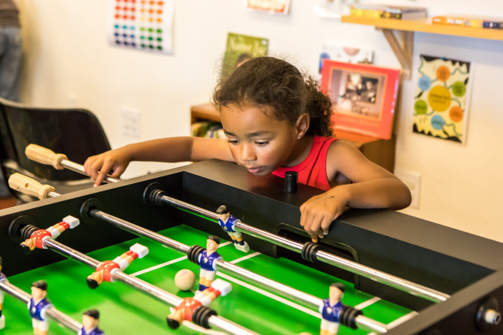 A child with their hair pulled back leans over a foosball table.